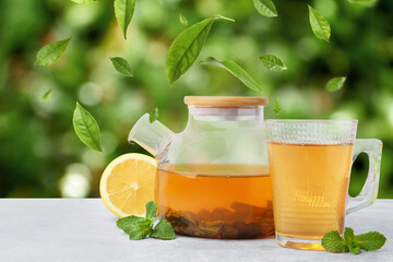 Green tea leaves flying above hot beverage on white table outdoors