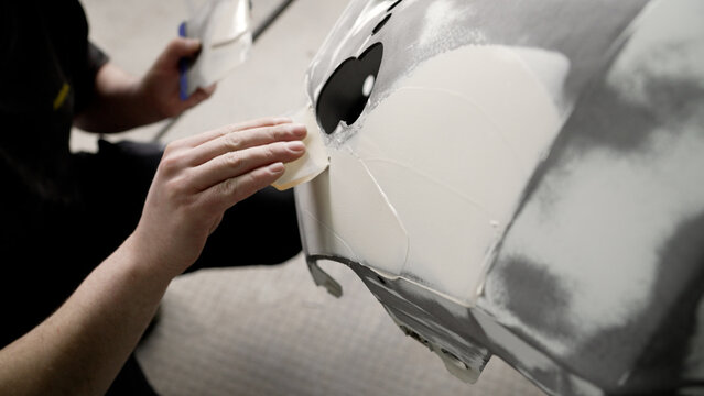 Auto body worker sanding putty on car bumper repairing vehicle