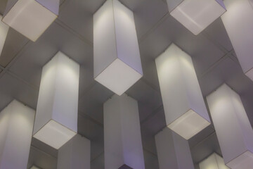 Modern ceiling design with geometric hanging light fixtures in a grid pattern, creating a minimalist architectural aesthetic in an indoor space.