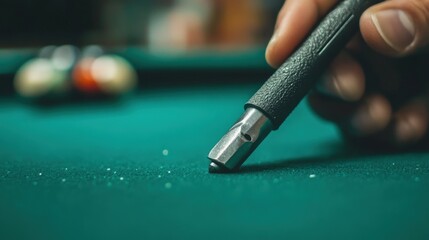 Close-up of a pool cue tip near pool balls on a green table.