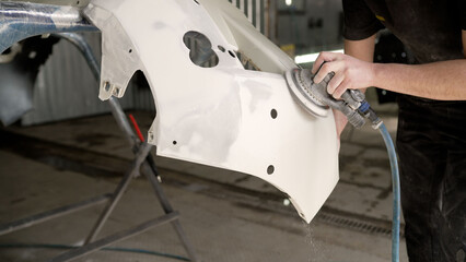 Mechanic polishing car bumper in auto repair shop
