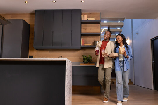 Walking African American couple carrying takeout box and disposable cups in kitchen, copy space