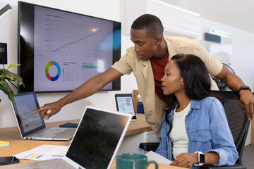 Collaborating African American coworkers analyzing charts on laptops in modern office, with mug