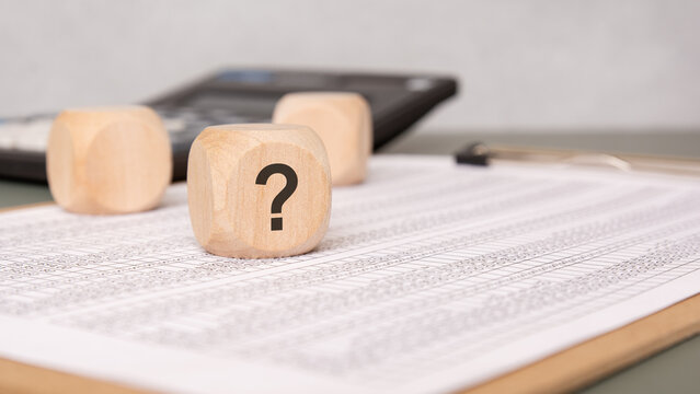 Wooden block with question mark on financial document, symbolizing uncertainty
