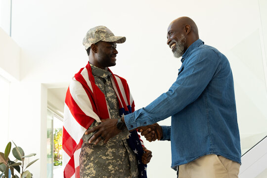 Shaking hands African American father and son at home, with military uniform and American flag
