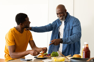 African American father and son preparing burgers in modern home kitchen, with buns and smartphone
