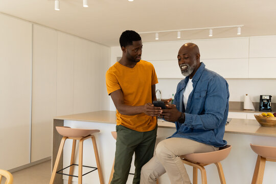 African American father and son sharing smartphone tips at kitchen island, with fruit bowl