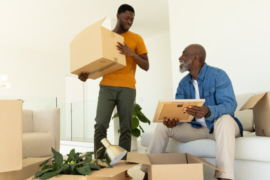 Unpacking African American father and son moving boxes in modern living room, with picture frame