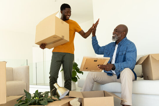 High-fiving African American father and son unpacking boxes in living room, with picture frame