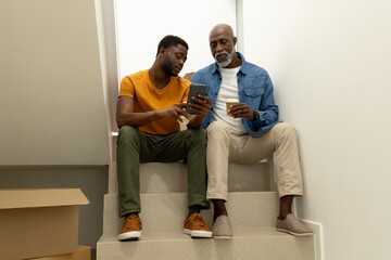 Sitting African American father and son browsing smartphone on staircase, with coffee cup and boxes