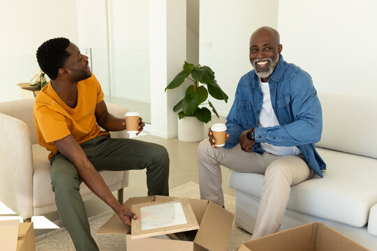 Unpacking African American father and son sitting in living room, with moving boxes, framed picture