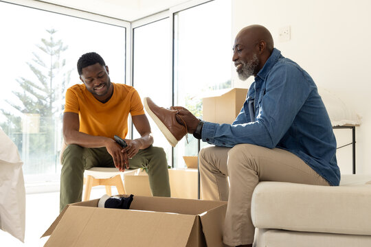 Unpacking African American father and son opening boxes in living room with shoe and smartphone