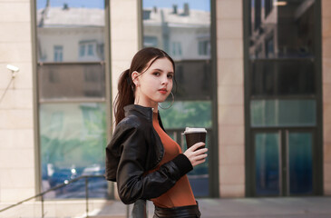Fototapeta premium Girl with hot coffee against the background of a modern city building.