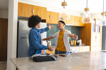 Smiling, Diverse male friends greeting each other in modern kitchen, with sling bag and smartphone