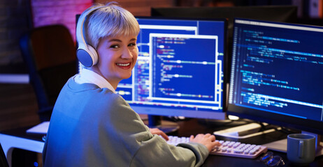 Female programmer with headphones working in office at night