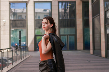 Fototapeta premium A girl with freckles in a leather skirt near a skyscraper.