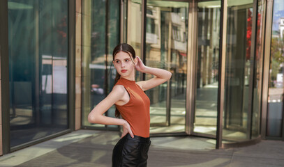 A girl with freckles in a leather skirt near a skyscraper.