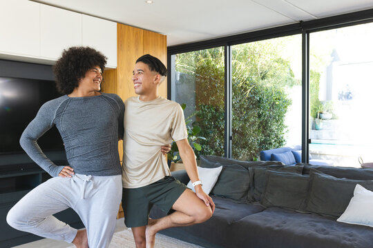 Balancing Diverse male friends practicing partner yoga in living room, with flat-screen TV - Powered by Adobe
