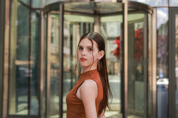 A girl with freckles in a leather skirt near a skyscraper.