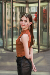 A girl with freckles in a leather skirt near a skyscraper.