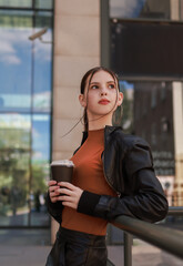 Obraz premium Girl with hot coffee against the background of a modern city building.