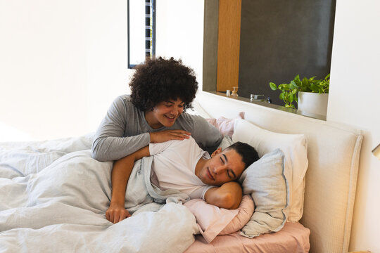 Resting Diverse male partners lying on bed in modern bedroom, with light duvet and potted plant - Powered by Adobe