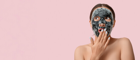 Surprised young woman with activated charcoal mask on her face against pink background