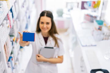 Female pharmacist holding up a box of medication in the pharmacy.