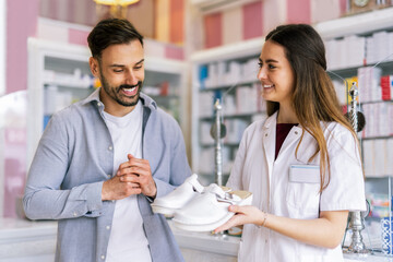 Obraz premium Pharmacist helping the customer choose white medical clogs at the pharmacy store.