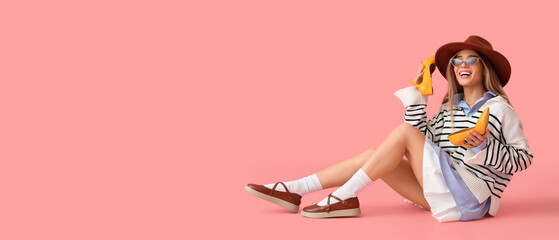 Stylish young woman in spring clothes with high heels sitting on pink background