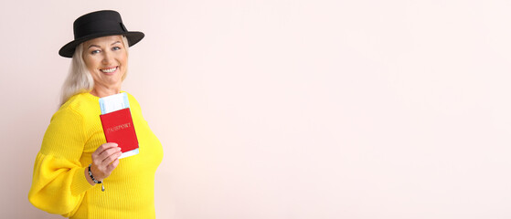 Happy mature woman with passport and ticket on light background
