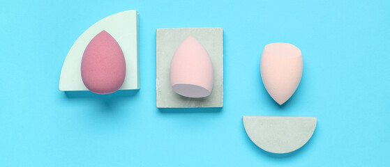 Decorative podiums with pink makeup sponges on blue background