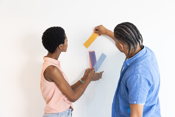 Diverse coworkers arranging paint swatches on white wall indoors, with pastel and bold tones