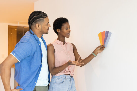 Diverse couple choosing paint colors in room at home, with colorful paint swatch cards