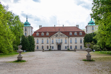 Palac w Nieborowie with red roof and decorative flowerbeds in the foreground on a spring day.