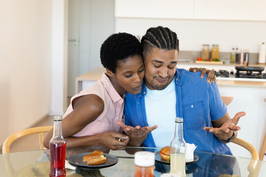 Tasting burgers diverse couple sitting at dining table in modern kitchen, with condiments - Powered by Adobe
