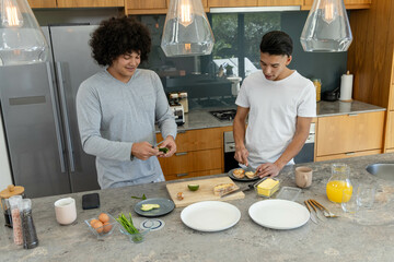 Chopping and spreading topping Diverse male friends at marble kitchen island, with avocado halves