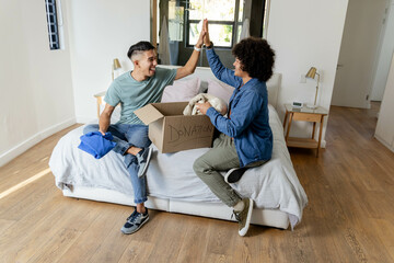 Sorting Diverse male friends placing folded clothes into cardboard donation box in modern bedroom