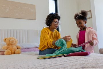 Sorting diverse mother and daughter arranging colorful folders on bed, with teal backpack