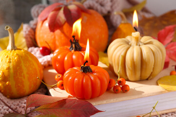 Beautiful composition with burning candles in shape of pumpkin, book and autumn leaves on windowsill