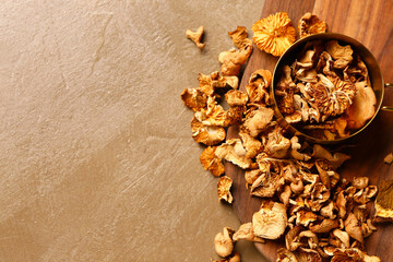 Saucepan and wooden board with tasty dried mushrooms on brown background