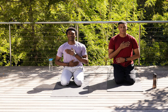 Kneeling diverse male friends practicing mindful breathing on deck terrace, with yoga mats