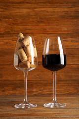 Glasses of red wine and corks on wooden background