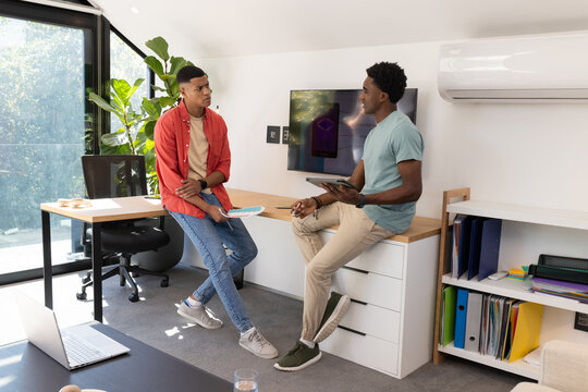 Discussing Diverse male coworkers exchanging ideas in home office, with laptop, tablet and notebook