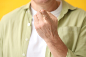 Mature man with contact lens on yellow background, closeup