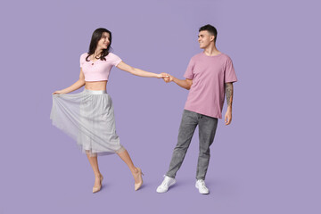 Beautiful young couple dancing on lilac background