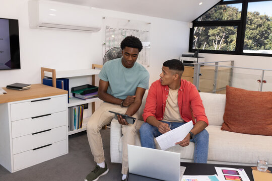 Diverse male coworkers reviewing documents on sofa in loft office, with tablet and swatch samples