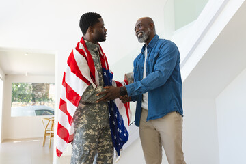 African American father and son hugging in home entryway, with soldier in camouflage draped in flag
