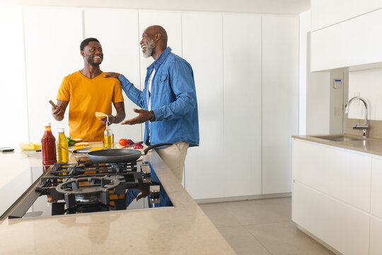 Cooking African American father and son at kitchen island, using spatula and smartphone, copy space