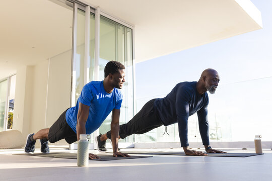 African American father and son planking on black mats in modern living area, with water bottles